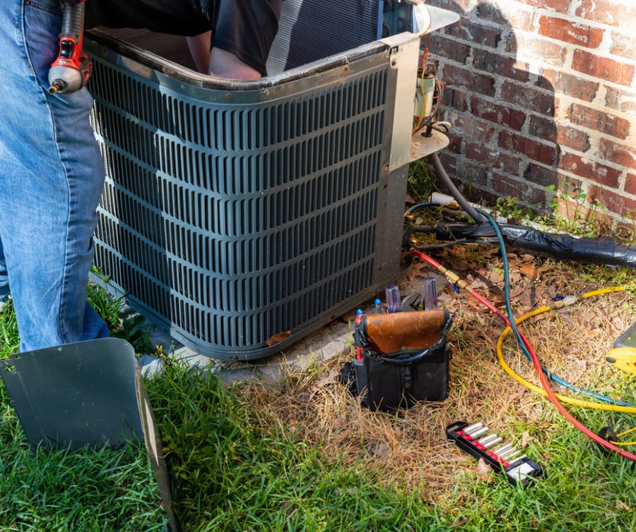 HVAC technician performing maintenance on outdoor unit. His tools are on the ground next to him.